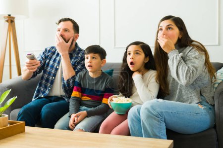 Téléchargez les photos : Surprised parents and kids watching a horror movie together and having fun eating popcorn - en image libre de droit