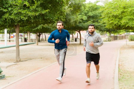 Téléchargez les photos : Full length of young men friends with a fitness and active lifestyle at the park running together - en image libre de droit