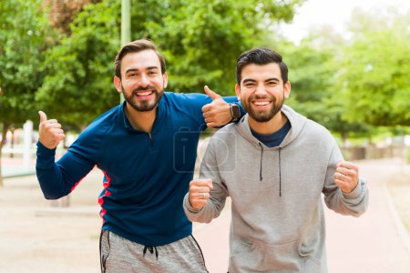 Photo for Attractive happy men friends doing a thumbs up and feeling excited about finishing their workout exercises outdoors - Royalty Free Image