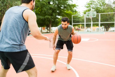 Photo for Active latin man playing a one on one game with a friend at the park basketball court - Royalty Free Image