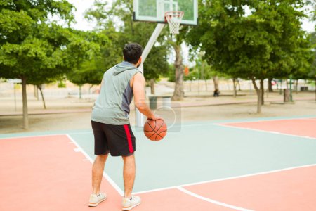 Téléchargez les photos : Fitness young man practicing basketball alone on the court and preparing to throw the ball into the hoop - en image libre de droit