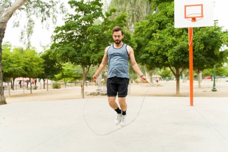 Téléchargez les photos : Caucasian man in his 30s doing cardio exercises while jumping rope during his fitness workout in the park - en image libre de droit