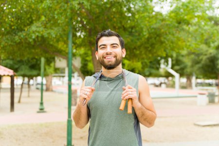 Téléchargez les photos : Portrait of a happy latin man smiling while using a jumping rope for his cardio workout outdoors - en image libre de droit
