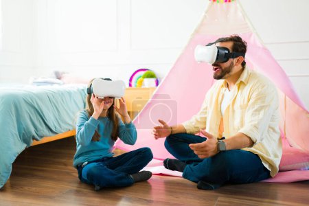 Foto de Excited father and elementary daughter playing videogames or watching virtual reality videos with glasses - Imagen libre de derechos