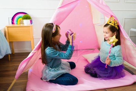 Photo for Beautiful kids best friends dressed as princesses taking photos with a toy camera while playing together - Royalty Free Image