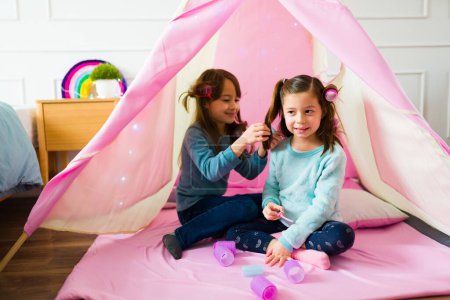 Adorable little girls and best friends playing in a pink teepee doing different hairstyles having fun