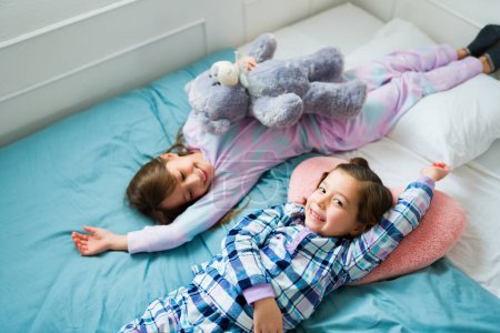 Photo for Cute caucasian girl having a fun sleepover with her best friend while resting in bed during the morning - Royalty Free Image