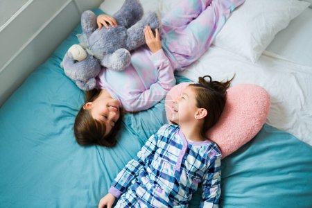 Photo for Cute kids and best friends in pajamas and a teddy bear laughing having a lot of fun during a sleepover - Royalty Free Image