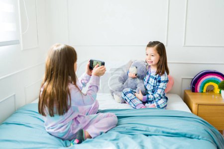 Foto de Caucasian child playing taking a photo of her best friend with a smartphone during a fun sleepover - Imagen libre de derechos