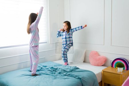 Foto de Beautiful happy kids having a best friend sleepover while dancing and jumping in bed together - Imagen libre de derechos
