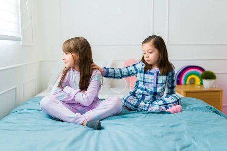 Foto de Sad little girl angry with her upset best friend during a sleepover while apologizing after having a fight - Imagen libre de derechos