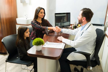 Téléchargez les photos : Mère latine souriant serrant la main du médecin tout en emmenant sa jeune fille chez le pédiatre - en image libre de droit