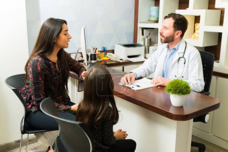 Photo for Hispanic mother talking with a pediatrician doctor about medical treatment for her sick young kid - Royalty Free Image