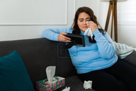 Téléchargez les photos : Obese woman crying wiping her tears with tissues because of her sad heartbroken breakup looking at the picture frame - en image libre de droit
