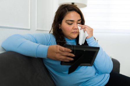 Foto de Upset sad overweight woman crying and using tissues while missing her ex partner after her breakup - Imagen libre de derechos