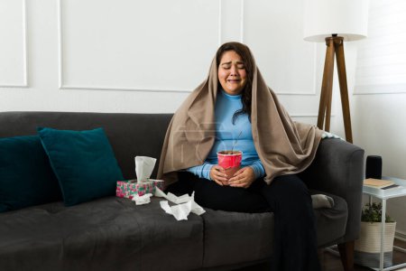 Foto de Triste mujer con sobrepeso llorando envuelta en una manta mientras comía helado de chocolate debido a su triste ruptura - Imagen libre de derechos