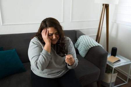 Foto de Mujer hispana deprimida llorando sintiéndose triste mientras mira su anillo de compromiso después de una ruptura desgarradora de su ex prometido - Imagen libre de derechos