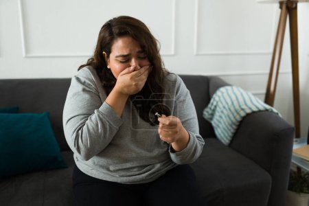 Foto de Triste mujer gorda triste llorando mirando su anillo de diamantes después de romper su compromiso con su prometido sintiéndose deprimida en casa - Imagen libre de derechos