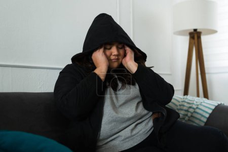 Téléchargez les photos : Stressed sad overweight woman suffering a headache and depression after a breakup looking depressed wearing a black hoodie - en image libre de droit