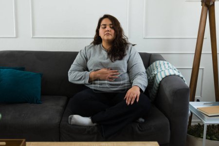 Téléchargez les photos : Overweight hispanic woman relaxing meditating and doing breathing exercises to prevent anxiety - en image libre de droit