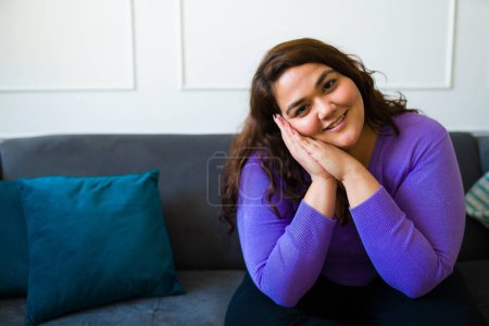 Photo for Beautiful hispanic woman looking happy smiling with her hands on the face while sitting on the sofa - Royalty Free Image