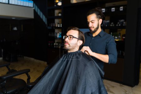 Foto de Hombre guapo en la peluquería cortándose el pelo y consiguiendo un nuevo corte de pelo con un estilista hispano masculino - Imagen libre de derechos