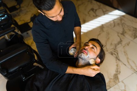 Foto de Top view of a caucasian man getting ready for grooming services while shaving his beard with a barber - Imagen libre de derechos