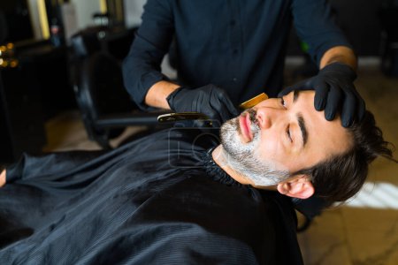 Foto de Attractive caucasian man at the barber shop or salon getting grooming services and shaving his beard - Imagen libre de derechos