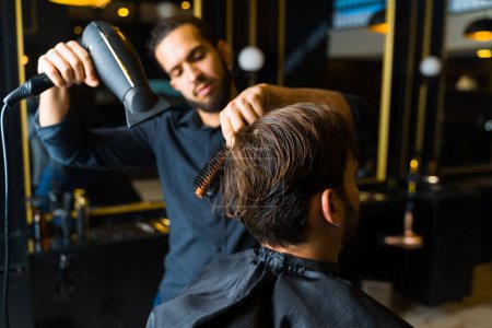 Photo for Close up of a male hairstylist using a blow dryer and a brush after cutting the hair of a man customer at the salon - Royalty Free Image