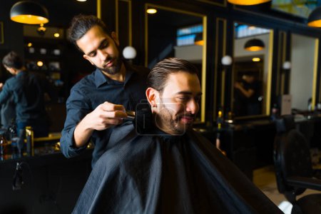 Foto de Happy male customer smiling while getting a new trendy haircut at an elegant barber shop or hair salon - Imagen libre de derechos
