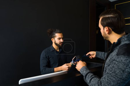 Téléchargez les photos : Caucasian man client paying with a credit card for a hair cut or grooming services at the elegant barber shop - en image libre de droit
