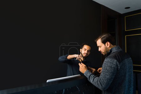 Foto de Trabajador latino mostrando el menú de servicios a un cliente masculino que viene a la peluquería o peluquería profesional con espacio para copias - Imagen libre de derechos