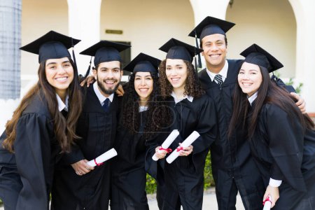Photo for Cheerful friends graduates wearing graduation gowns and caps smiling and making eye contact after receiving their diploma - Royalty Free Image