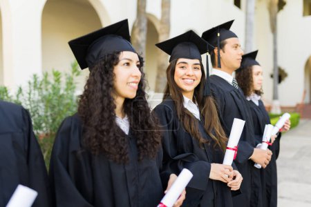 Téléchargez les photos : Les jeunes femmes lors de leur cérémonie de remise des diplômes souriant faire contact avec les yeux et l'air heureux tout en recevant leurs diplômes universitaires - en image libre de droit