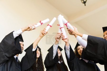 Téléchargez les photos : Angle bas d'un groupe de diplômés montrant leurs diplômes universitaires après leur cérémonie de remise des diplômes - en image libre de droit