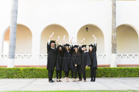 Photo for Full length of a group of friends graduates at college campus celebrating after receiving their university diplomas at their graduation - Royalty Free Image