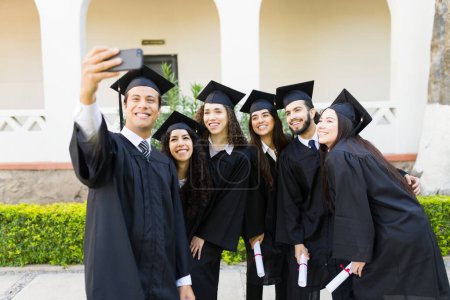 Téléchargez les photos : Jeune homme latino prenant un selfie avec ses amis après avoir reçu leur diplôme lors de leur cérémonie de remise des diplômes - en image libre de droit
