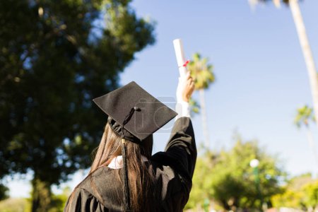 Téléchargez les photos : Vue arrière d'une jeune diplômée vue de derrière avec sa robe de fin d'études montrant son diplôme universitaire - en image libre de droit
