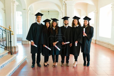Téléchargez les photos : Pleine longueur de femmes et d'hommes posant avec leurs robes et casquettes de fin d'études après avoir reçu leur diplôme universitaire - en image libre de droit