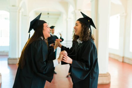 Foto de Super excited best friends holding hands and screaming with happiness during their graduation ceremony at college campus - Imagen libre de derechos