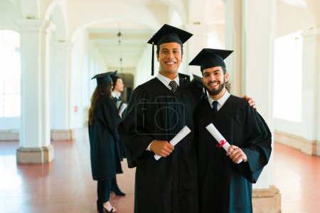 Téléchargez les photos : Beaux jeunes hommes latins souriants rendant le contact visuel heureux lors de leur cérémonie de graduation unverstiy - en image libre de droit