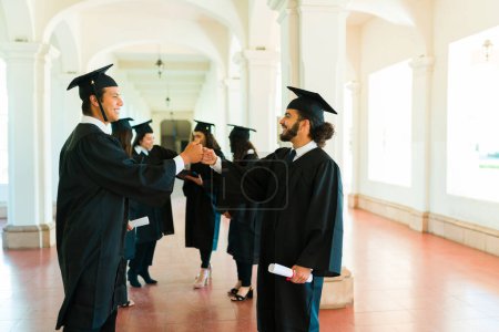 Foto de Latin mexican friends at university shaking hands and saying congratulations after their graduation ceremony - Imagen libre de derechos