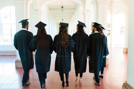 Téléchargez les photos : Vue arrière d'un groupe d'amis et de diplômés marchant ensemble sur le campus du collège avant la cérémonie de remise des diplômes - en image libre de droit
