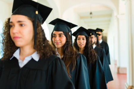Foto de Mujeres felices graduadas esperando en fila para obtener su diploma universitario en la ceremonia de graduación - Imagen libre de derechos