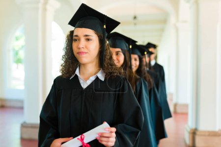 Photo for Beautiful woman with curly hair holding her diploma waiting in line during the graduation ceremony on campus - Royalty Free Image