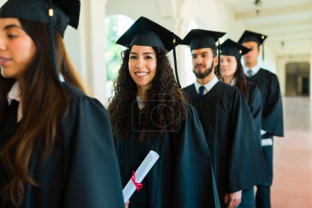 Photo for Attractive happy woman with curly hair smiling holding her university diploma waiting at the graduation ceremony with friends - Royalty Free Image
