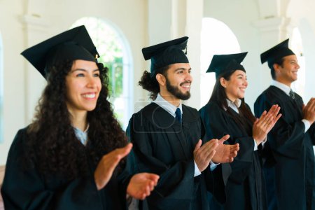 Photo for Cheerful attractive women and men graduates smiling while clapping during their university graduation ceremony - Royalty Free Image