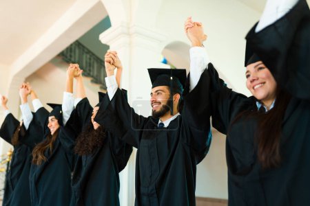 Photo for Cheerful young women and men with graduation gowns and caps celebrating together and smiling - Royalty Free Image