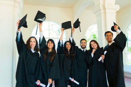 Téléchargez les photos : Attrayant groupe heureux d'amis jetant leurs casquettes de graduation dans l'air et célébrant - en image libre de droit
