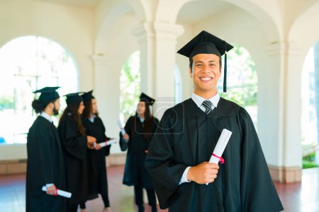 Téléchargez les photos : Heureux jeune homme hispanique se sentant fier et heureux d'avoir obtenu son diplôme et de terminer ses études collégiales - en image libre de droit